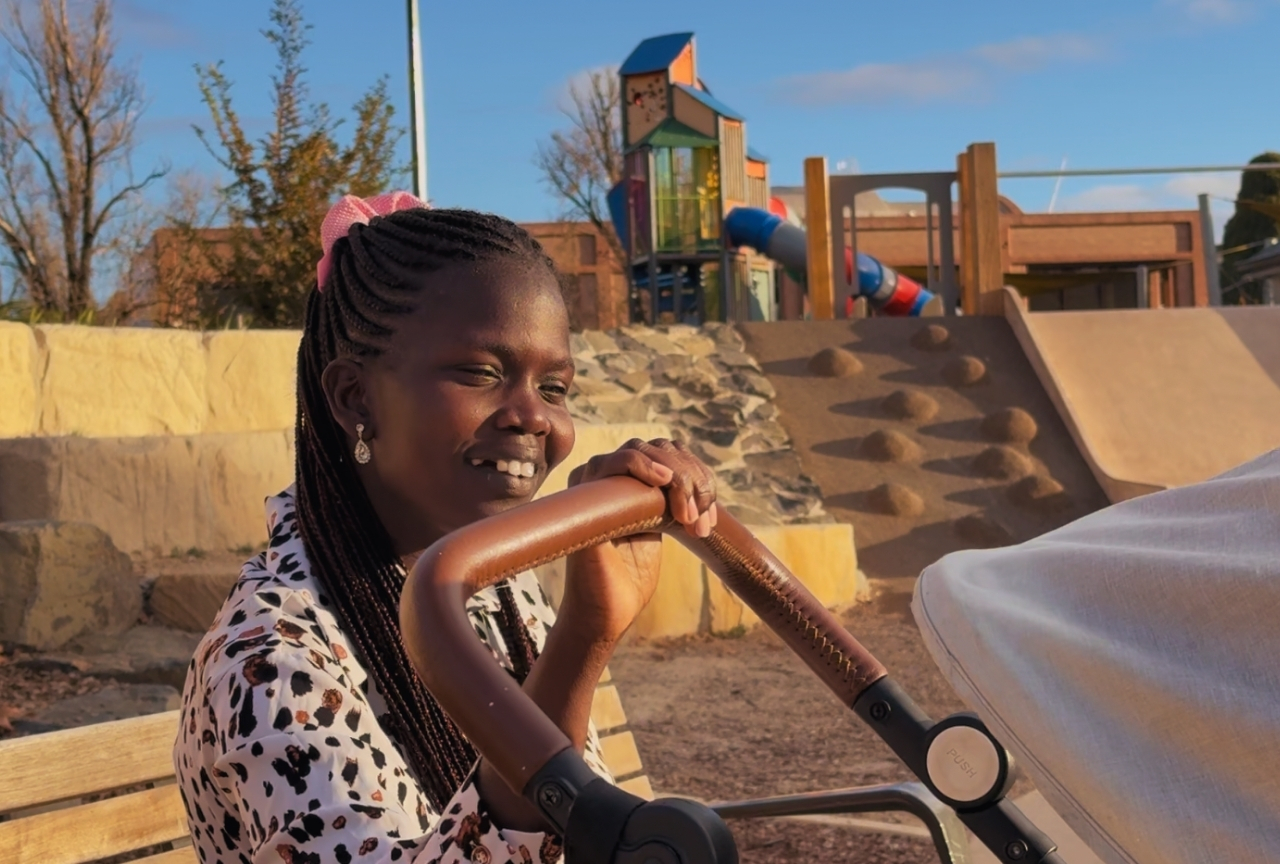 Akol smiling at a park in Armidale with a pram, golden afternoon light