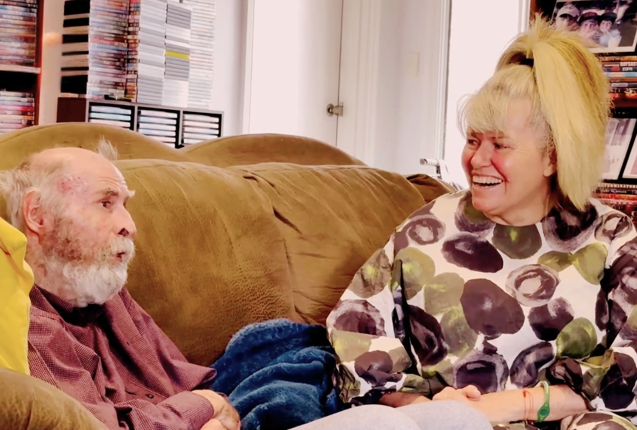 John Bell laughing with his daughter Vanessa Murray on the couch at home
