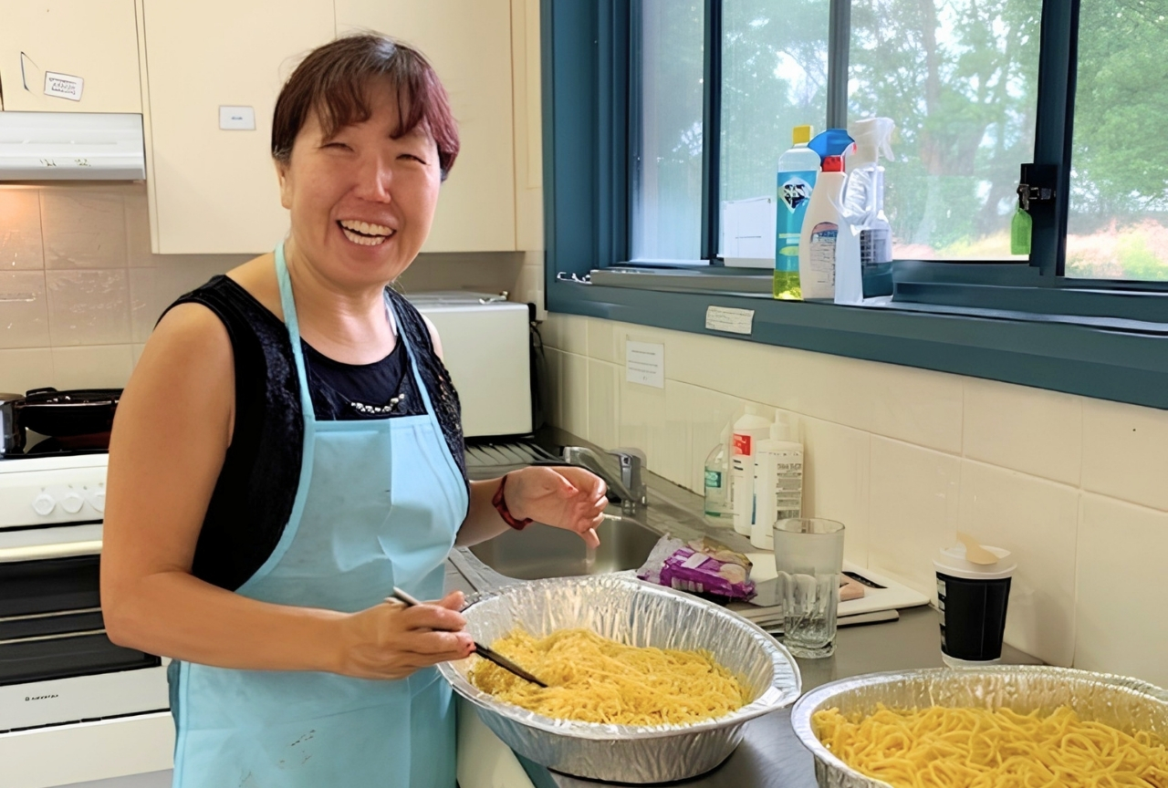 Sumie smiling while preparing noodles in the kitchen at a Japanese Family Group gathering